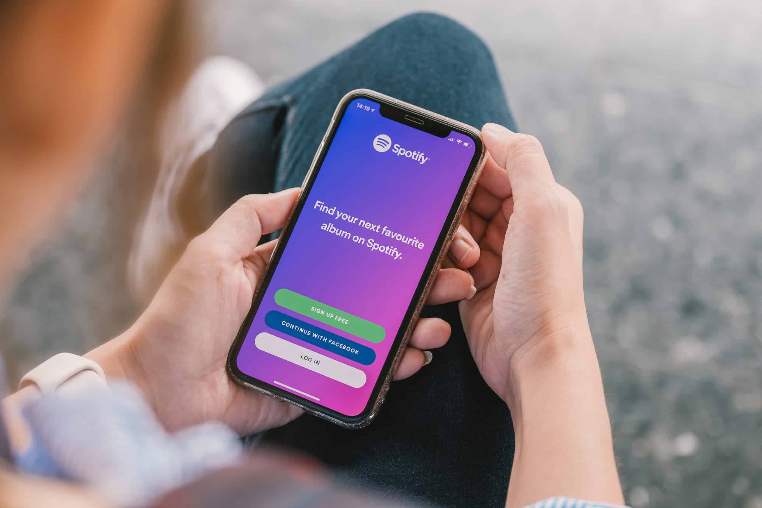 Woman hand holding iPhone Xs with Spotify login screen. Spotify is a music service that offers legal streaming music.