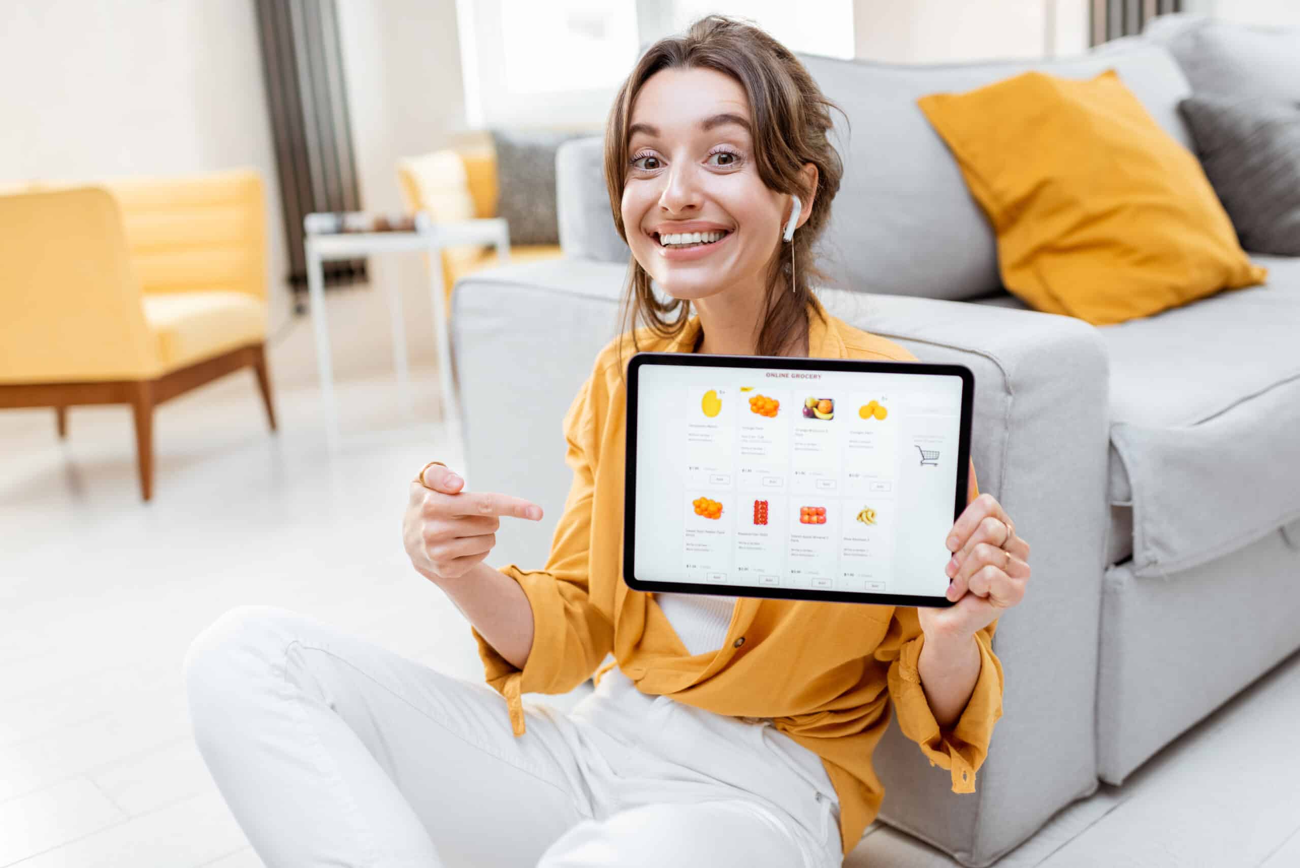 Young and cheerful woman showing a digital tablet screen with launched online store, shopping online at home. Concept of buying online using mobile devices
