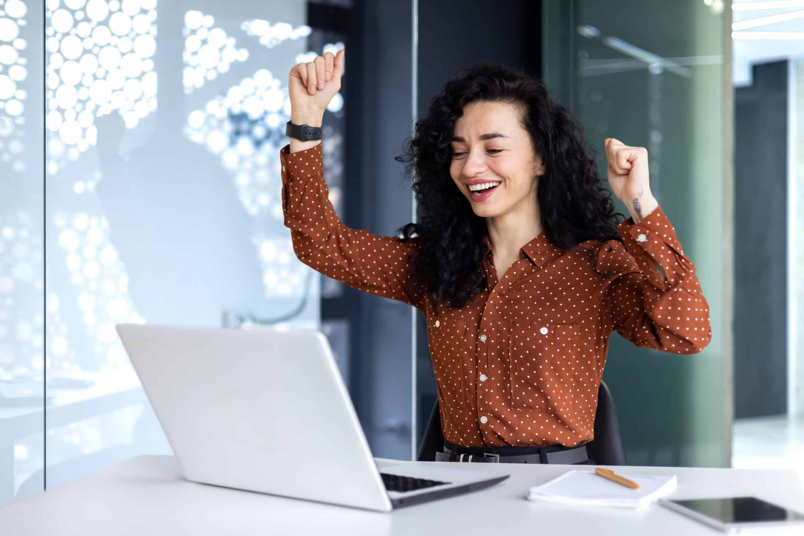 How Website Design Affects User Experience - Young hispanic business woman got good work result, business woman is happy and celebrating victory holding hands up looking and reading from laptop screen.