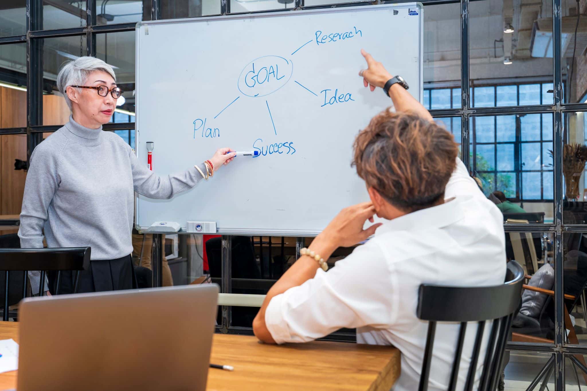 Senior business team leader is guiding young member to business success by showing chart for goal achievement for startup and creativity project concept