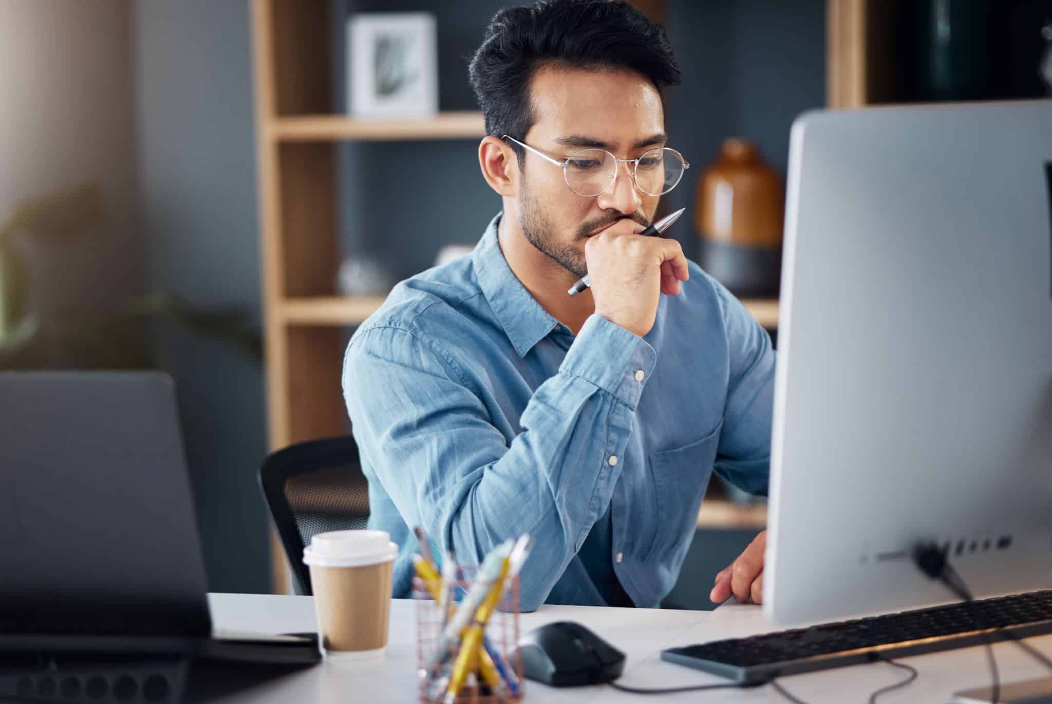 Young male with hand on chin using computer at desk in creative office