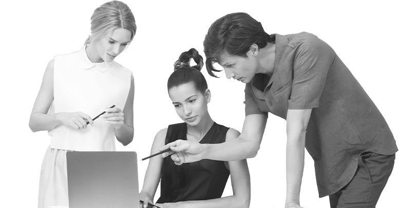 Black and white image of three women in business attire, collaboratively working over a laptop. One stands pensively with a stylus, another is pointing at the laptop screen, and the third is leaning in to look closer.